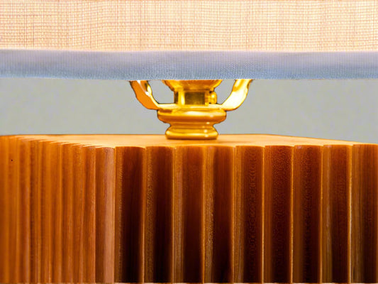 Detail of corner of tall square fluted table lamp with rectangular linen shade on white background showing brass fittings